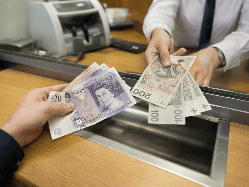 Wymiana funtów brytyjskich na złotówki – jedna ręka podaje banknoty GBP, druga banknoty PLN, w kantorze w Warszawie